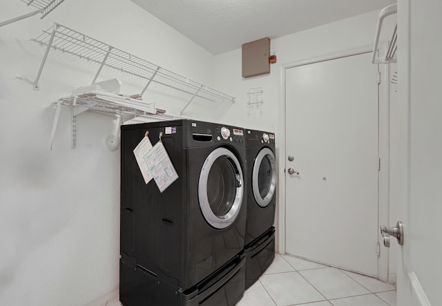 laundry area featuring light tile patterned flooring, a textured ceiling, and washing machine and clothes dryer