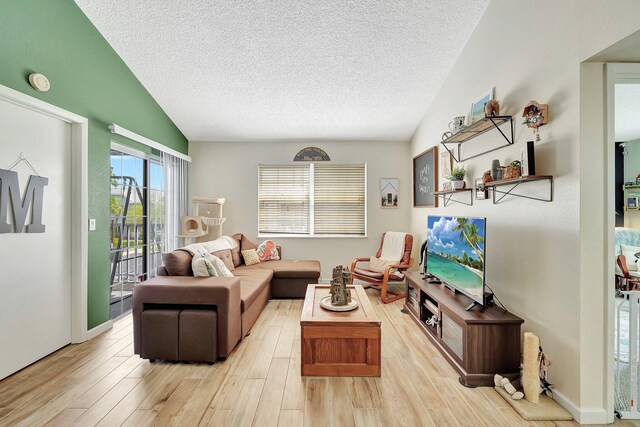 living room with a textured ceiling, light hardwood / wood-style flooring, and lofted ceiling