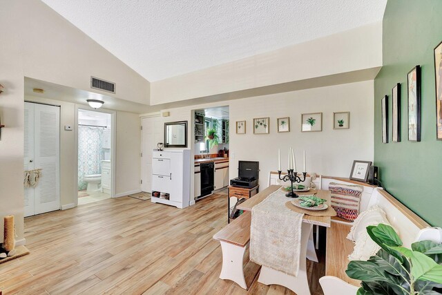 dining area with high vaulted ceiling, light wood-type flooring, and a textured ceiling