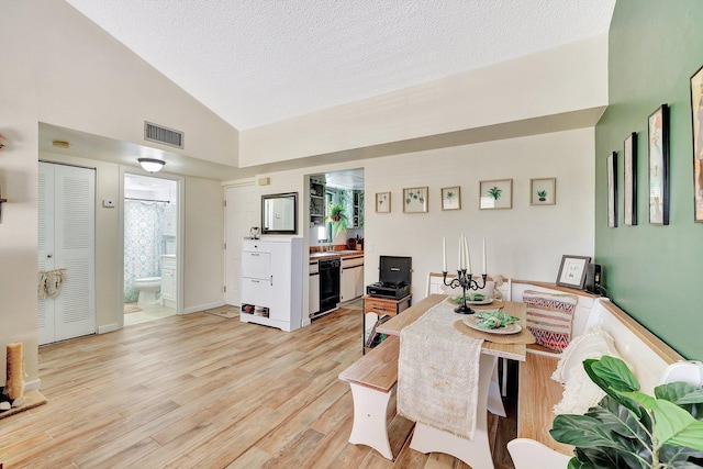 living room with vaulted ceiling, a textured ceiling, and light wood-type flooring