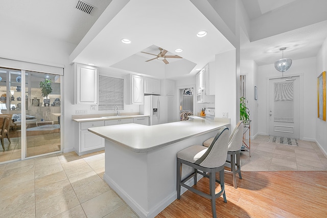 kitchen with sink, light wood-type flooring, kitchen peninsula, decorative light fixtures, and white cabinets