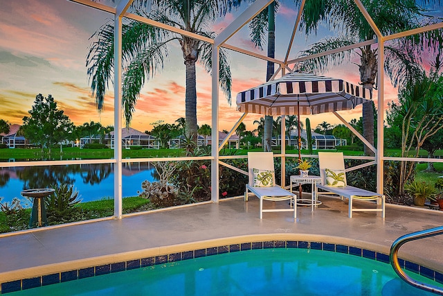 pool at dusk featuring a patio, a water view, and glass enclosure