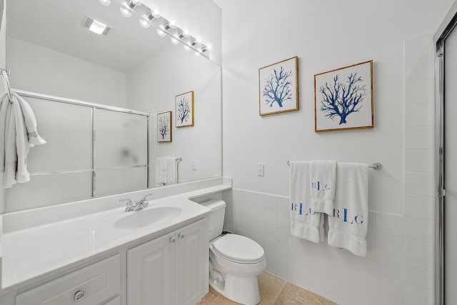 bathroom featuring a shower with door, tile walls, toilet, vanity, and tile patterned flooring