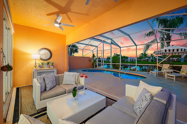 pool at dusk featuring glass enclosure, a patio, an outdoor hangout area, ceiling fan, and a water view