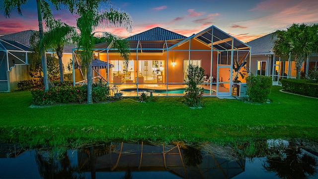 back house at dusk featuring a yard, a patio, a lanai, and a fenced in pool