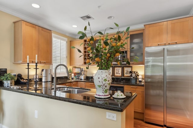 kitchen with kitchen peninsula, stainless steel refrigerator, sink, ornamental molding, and dark stone countertops