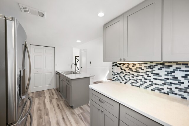 kitchen with kitchen peninsula, stainless steel appliances, light hardwood / wood-style floors, sink, and gray cabinetry