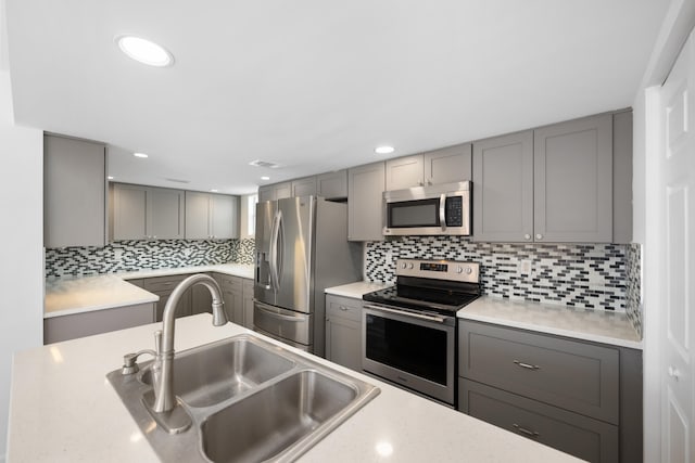 kitchen featuring sink, tasteful backsplash, stainless steel appliances, and gray cabinetry