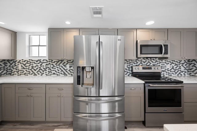 kitchen featuring gray cabinets, light hardwood / wood-style floors, backsplash, and stainless steel appliances