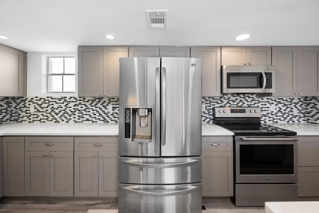 kitchen featuring gray cabinetry, stainless steel appliances, visible vents, light countertops, and tasteful backsplash