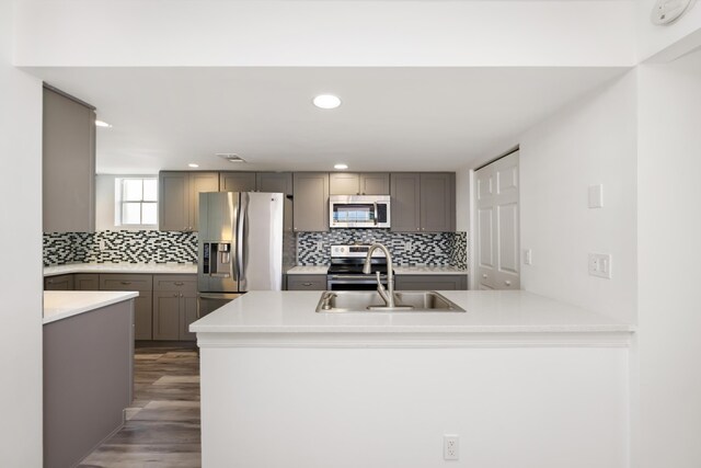 kitchen with appliances with stainless steel finishes, gray cabinetry, sink, decorative backsplash, and dark hardwood / wood-style floors