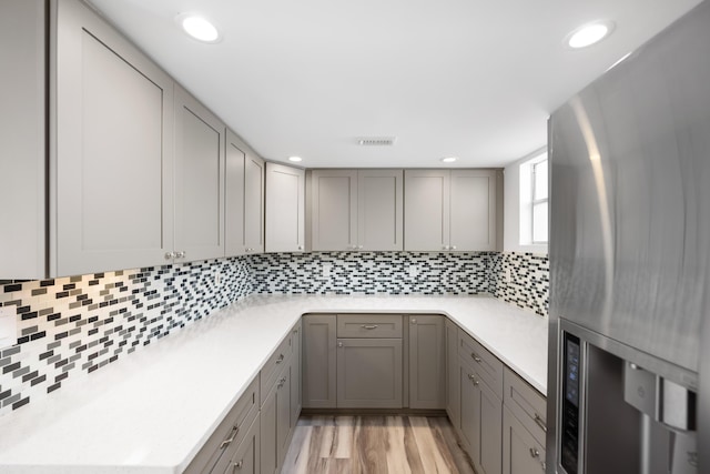 kitchen with recessed lighting, gray cabinets, decorative backsplash, light wood-type flooring, and stainless steel fridge with ice dispenser