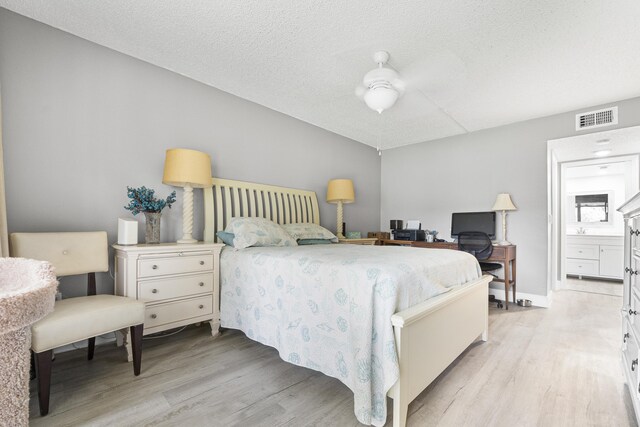 bedroom featuring light hardwood / wood-style flooring, ensuite bath, and a textured ceiling