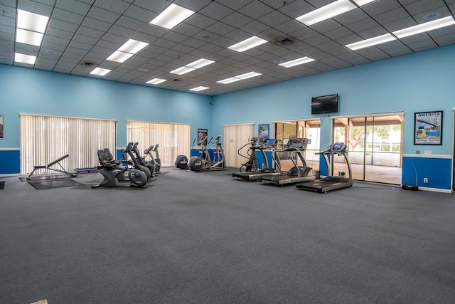 exercise room featuring a paneled ceiling, carpet, and a towering ceiling