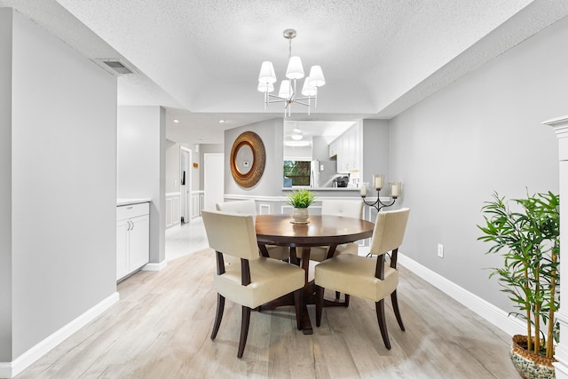 dining room with a notable chandelier, light hardwood / wood-style flooring, and a textured ceiling