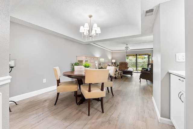 dining room featuring a raised ceiling, a textured ceiling, ceiling fan with notable chandelier, and light wood-type flooring