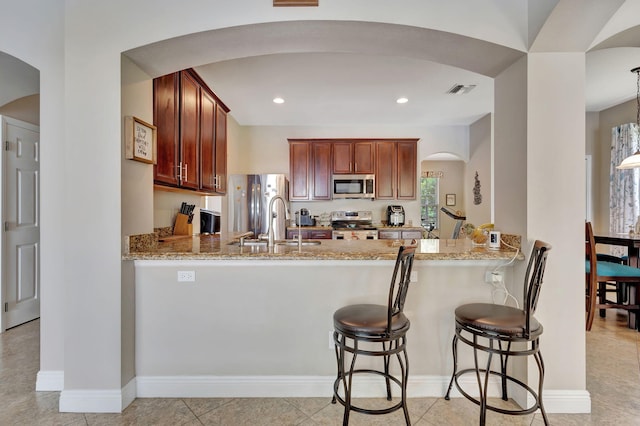 kitchen with light stone countertops, pendant lighting, appliances with stainless steel finishes, sink, and kitchen peninsula