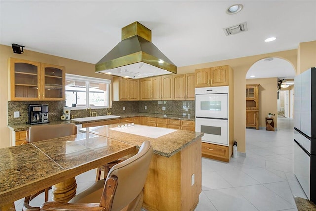 kitchen featuring white appliances, island range hood, vaulted ceiling, backsplash, and sink