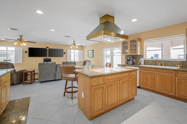 kitchen with a center island, island range hood, light stone countertops, sink, and a kitchen breakfast bar