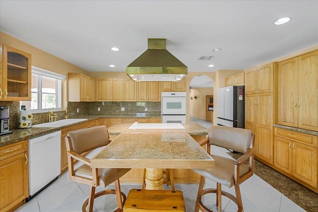 kitchen with white appliances, light tile patterned floors, backsplash, island exhaust hood, and sink