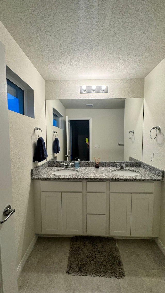 bathroom featuring tile patterned flooring, a textured ceiling, and dual bowl vanity