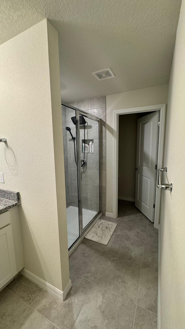 bathroom with tile patterned flooring, a textured ceiling, a shower with door, and vanity