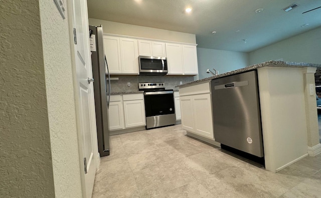 kitchen featuring dark stone countertops, decorative backsplash, light tile patterned floors, stainless steel appliances, and white cabinets