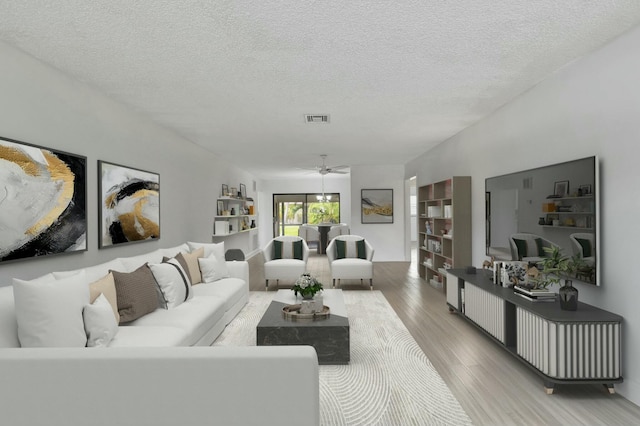 living room with ceiling fan, a textured ceiling, and light wood-type flooring