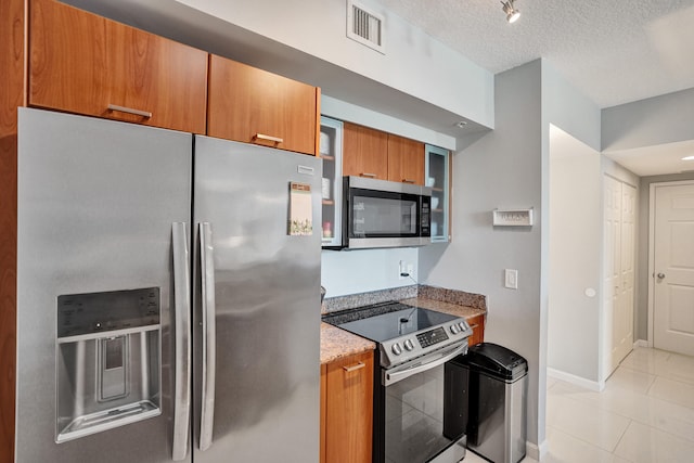 kitchen with track lighting, a textured ceiling, light tile patterned floors, and stainless steel appliances