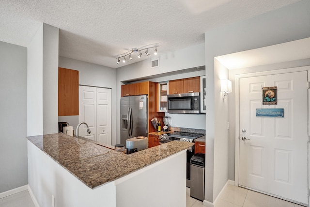 kitchen with appliances with stainless steel finishes, kitchen peninsula, rail lighting, and a textured ceiling