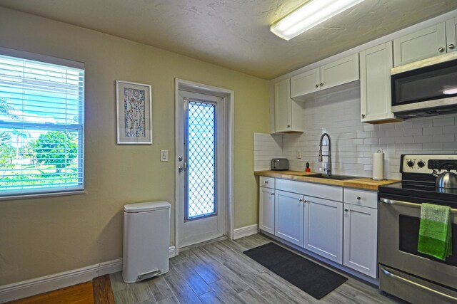 kitchen with stainless steel appliances, decorative backsplash, butcher block countertops, sink, and plenty of natural light