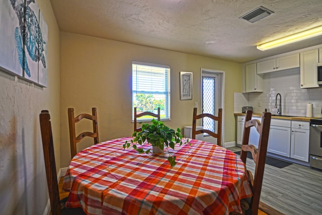 dining room with sink, a textured ceiling, and hardwood / wood-style flooring