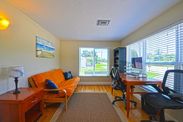 home office with light hardwood / wood-style floors and a textured ceiling