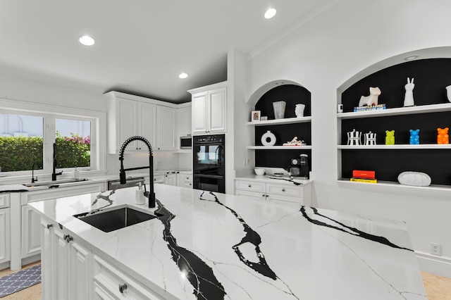 kitchen with double oven, light stone counters, sink, and white cabinetry