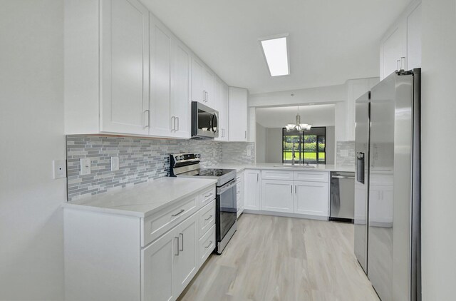 kitchen with an inviting chandelier, appliances with stainless steel finishes, tasteful backsplash, white cabinets, and sink