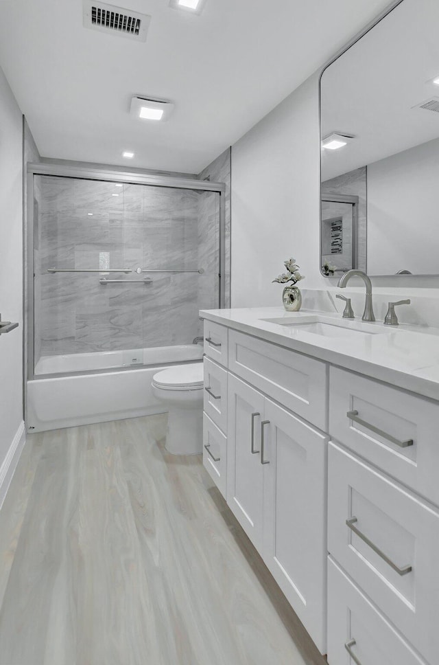 full bathroom featuring toilet, combined bath / shower with glass door, hardwood / wood-style flooring, and vanity