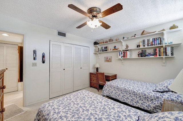 bedroom featuring a textured ceiling, light colored carpet, a closet, and ceiling fan