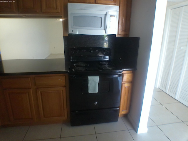 9872 Marina Blvd Unit 1434, Boca Raton, FL 33433 - kitchen featuring white microwave, black range with electric cooktop, light tile patterned flooring, and brown cabinets