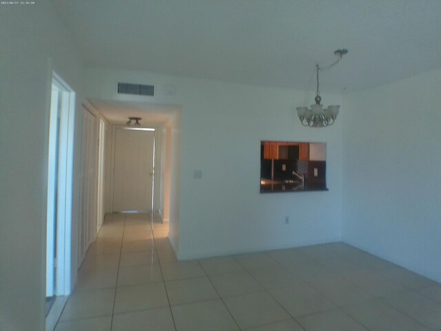 tiled spare room featuring a chandelier