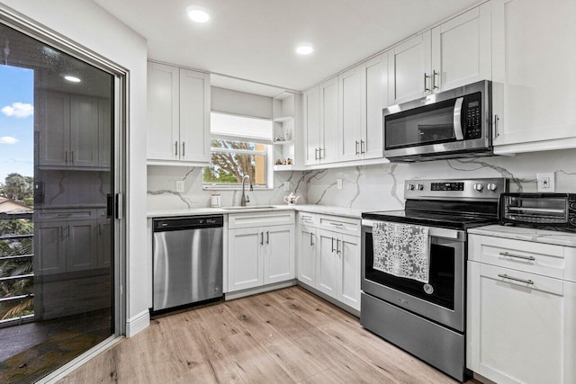 kitchen with sink, light wood-type flooring, white cabinets, stainless steel appliances, and backsplash