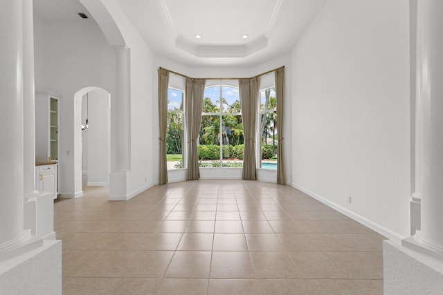 tiled empty room featuring a raised ceiling, ornamental molding, and ornate columns