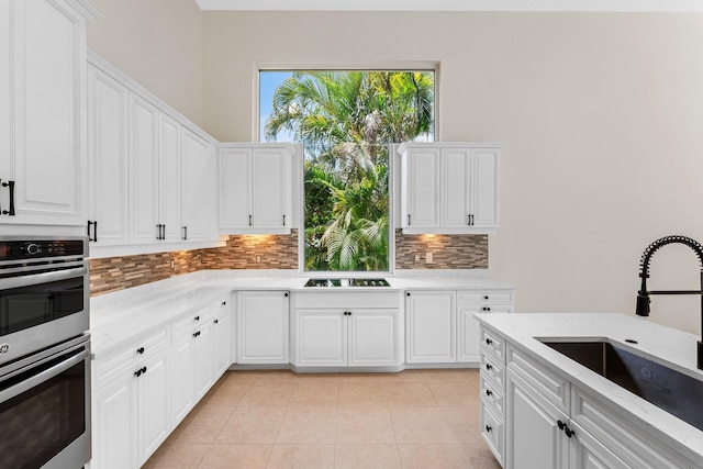 kitchen with white cabinets, stainless steel double oven, light stone countertops, and sink