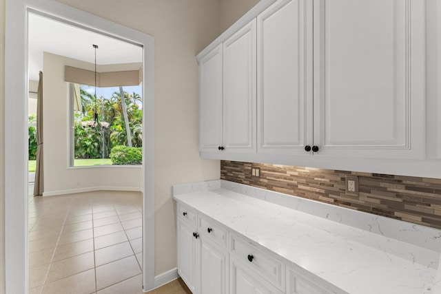 kitchen with backsplash, light stone countertops, light tile patterned flooring, and white cabinetry