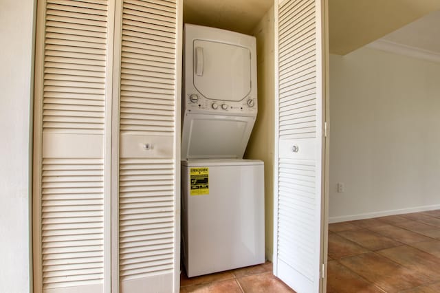 laundry room with light tile patterned floors, ornamental molding, and stacked washing maching and dryer