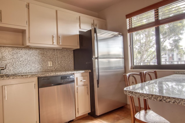 kitchen featuring tasteful backsplash, light stone countertops, appliances with stainless steel finishes, and light tile patterned floors