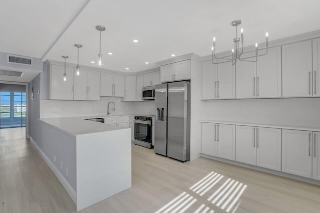 kitchen featuring white cabinets, kitchen peninsula, pendant lighting, light wood-type flooring, and appliances with stainless steel finishes