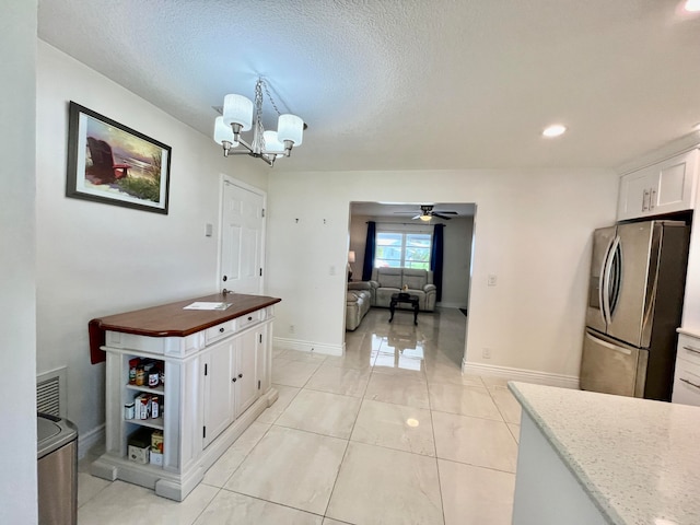 kitchen featuring white cabinets, light stone countertops, ceiling fan with notable chandelier, stainless steel refrigerator with ice dispenser, and light tile patterned flooring