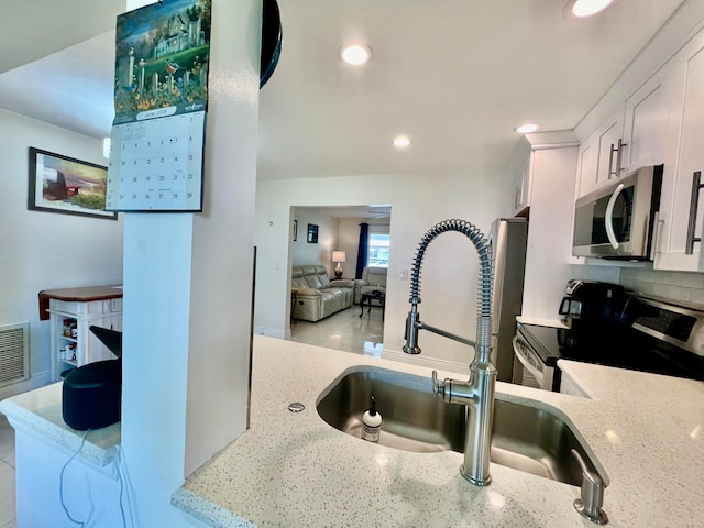 kitchen with appliances with stainless steel finishes, white cabinetry, light stone countertops, and sink