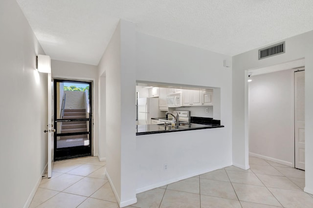 kitchen with white appliances, sink, light tile patterned floors, a textured ceiling, and white cabinetry