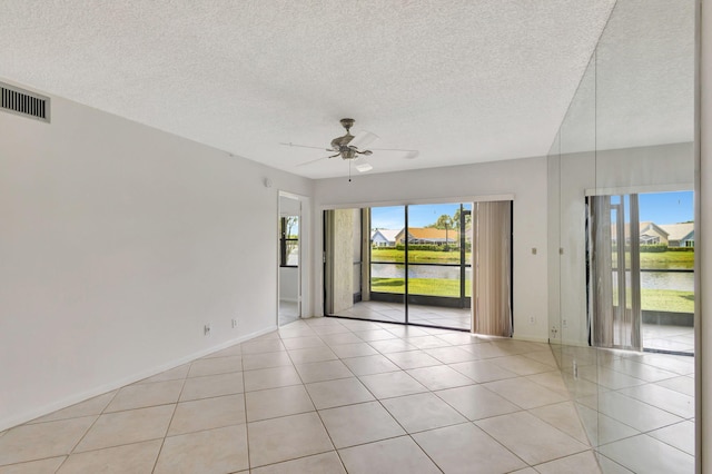 empty room with a textured ceiling, a water view, light tile patterned floors, and ceiling fan